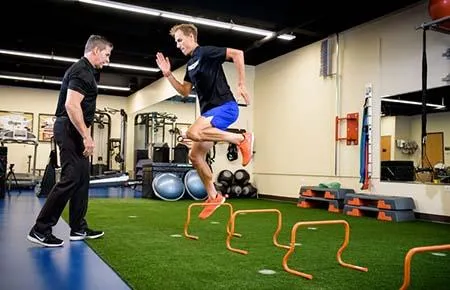 Athlete performing hurdle jump drills under the supervision of a sports performance coach.